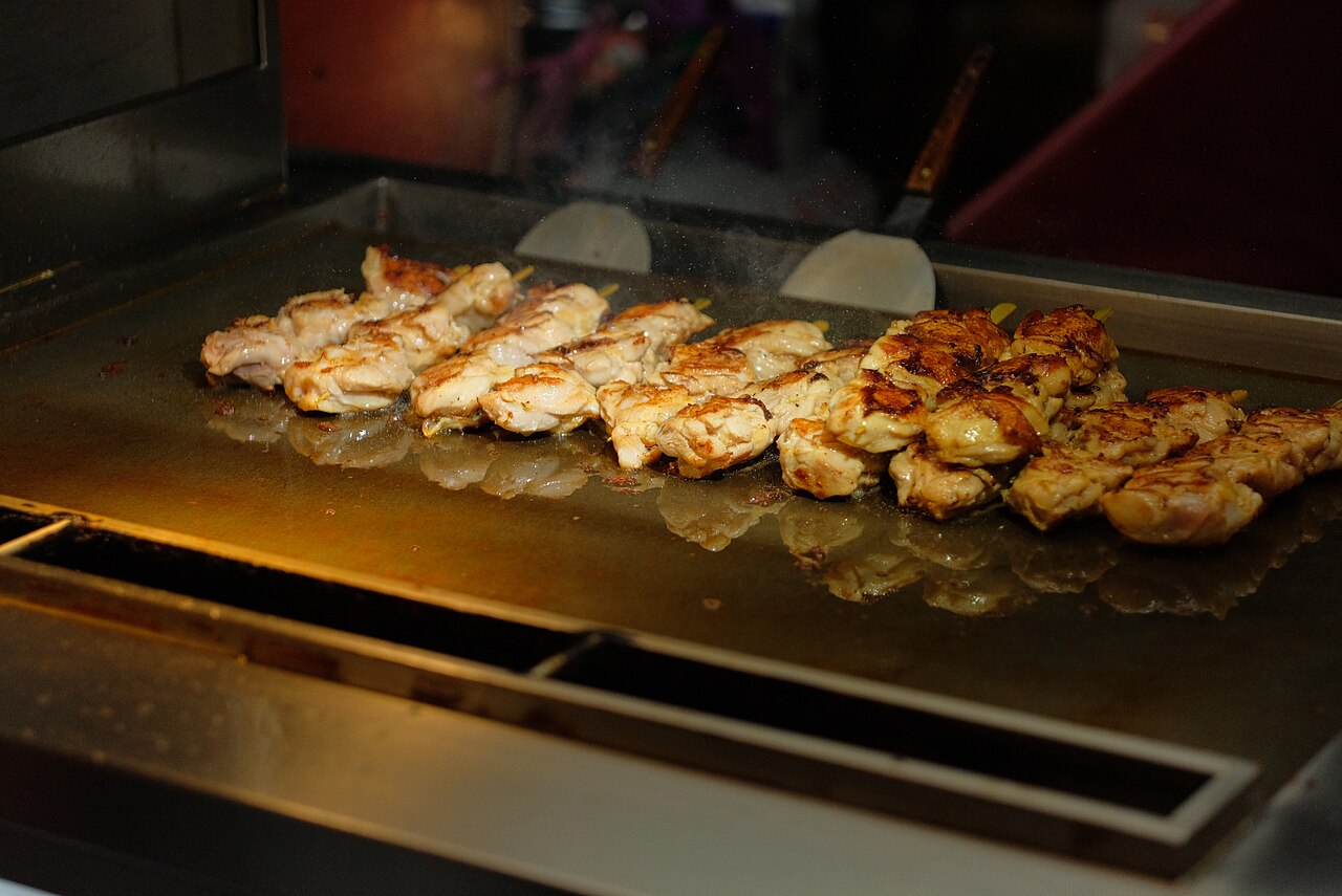 Brochetas de pollo asándose sobre una plancha caliente en un puesto del mercado nocturno de Shilin