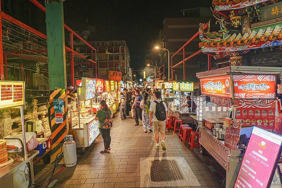 Calle del mercado nocturno de Shilin, llena de puestos iluminados y de gente paseando