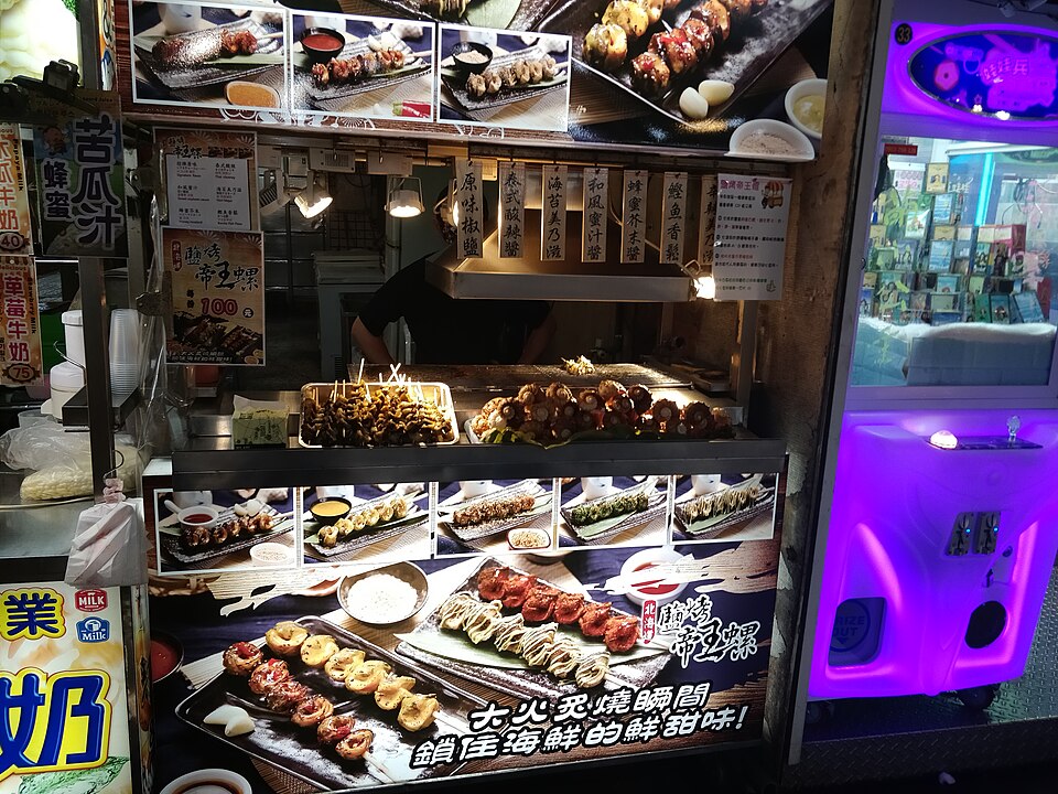 Puesto de marisco a la plancha en el mercado nocturno de Shilin, con carteles fotográficos de los platos